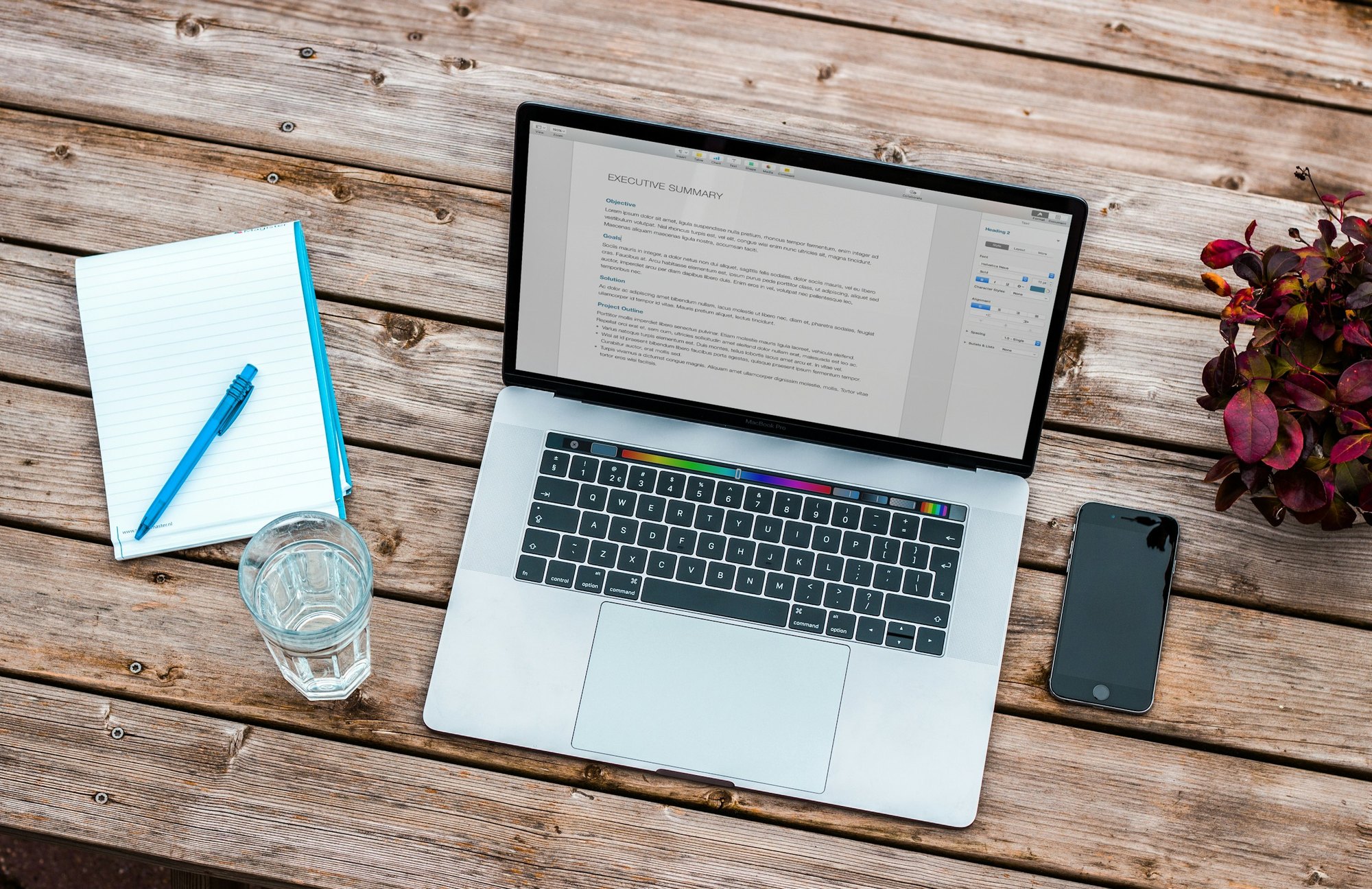 A laptop, notebook and phone on a wooden desk